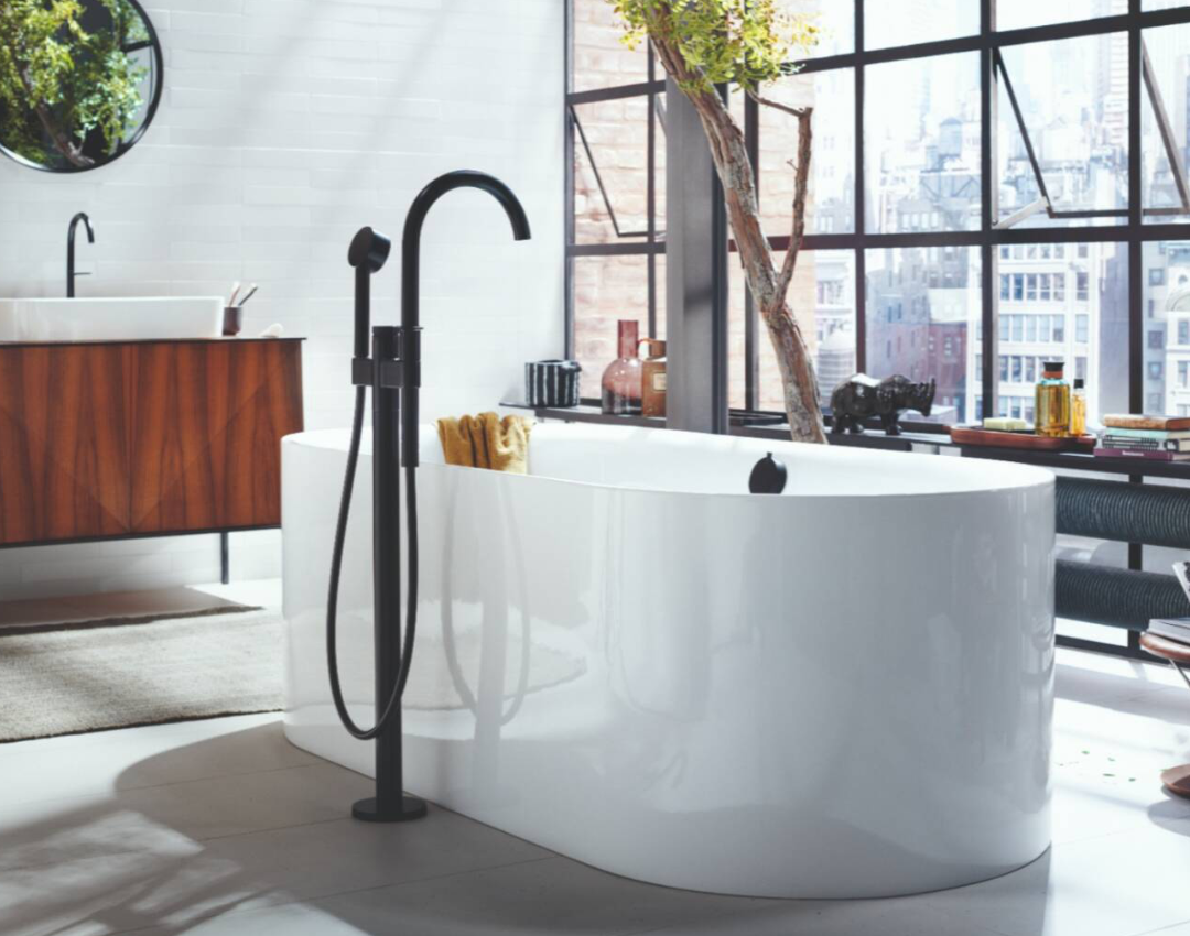 AXOR Uno floor-standing matte black bath mixer with handheld spray and white freestanding bathtub in an industrial loft bathroom