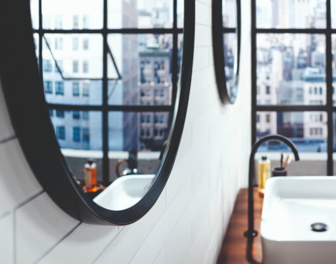 AXOR Uno matte black high-neck basin mixer with circular mirrors and industrial Crittall-style windows in a loft bathroom