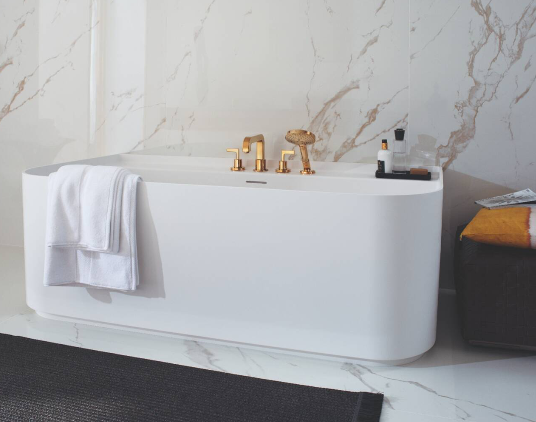 AXOR Citterio gold 4-hole deck-mounted bath mixer and handset on a white freestanding bathtub with marble wall backdrop