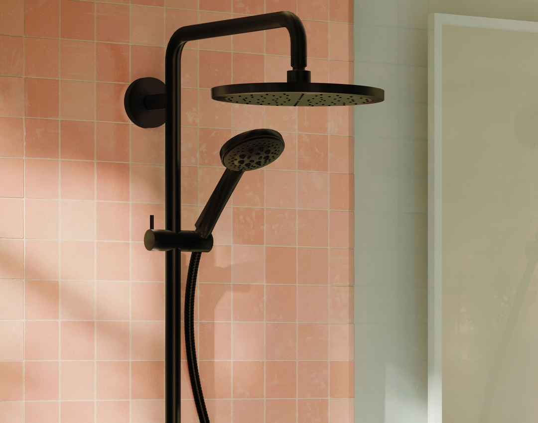 Dornbracht dark platinum matte shower system featuring a large round rainfall shower head and matching hand shower against pink square tiles.