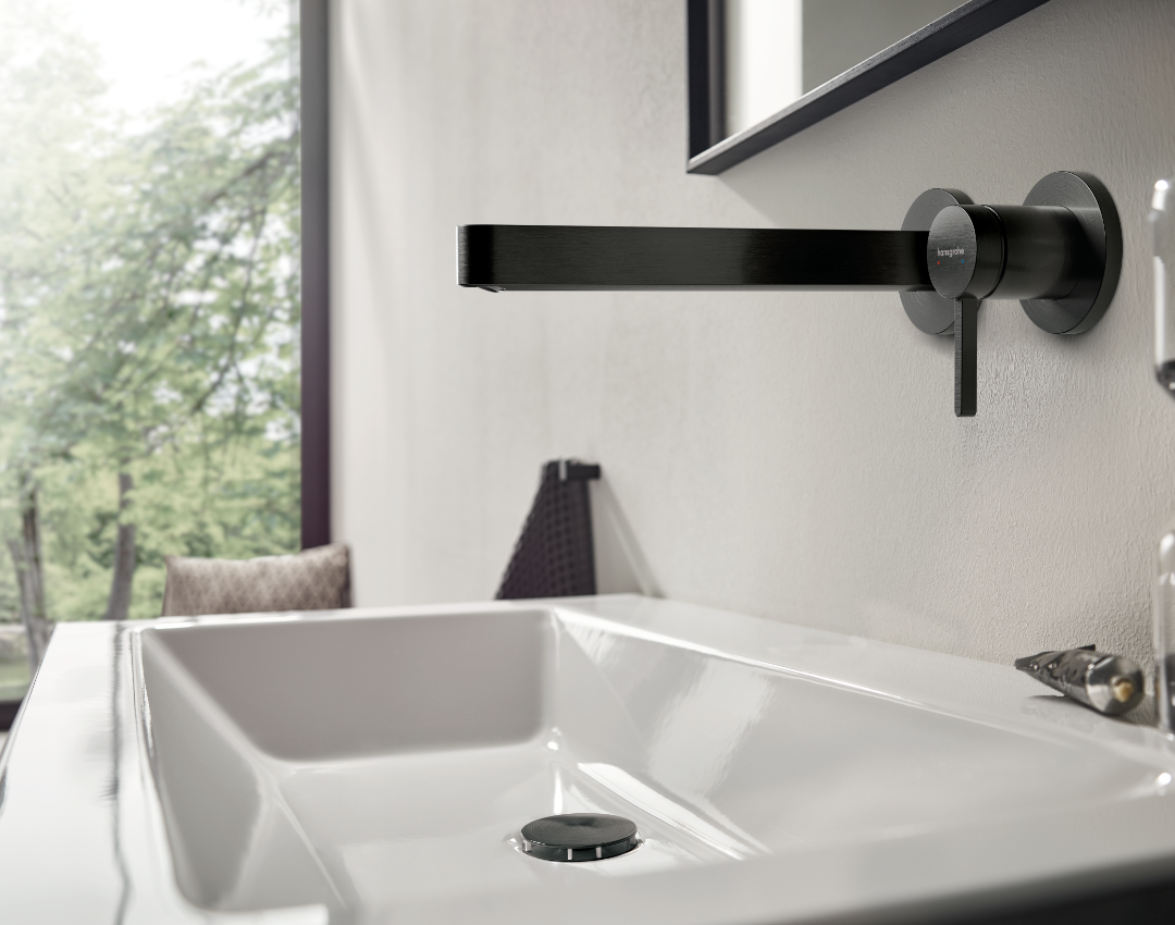 Hansgrohe wall-mounted matte black basin tap with long spout. Minimalist black bathroom brassware paired with a white countertop washbasin and black pop-up waste.