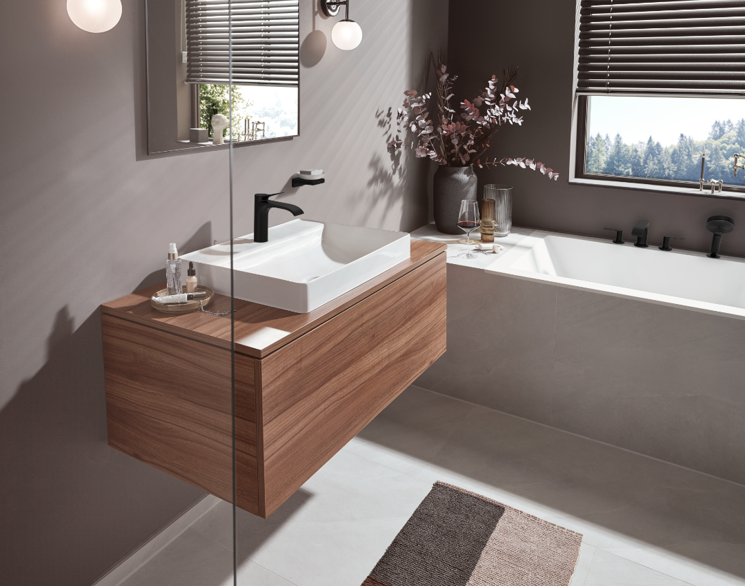 Contemporary hansgrohe bathroom furniture featuring a floating walnut-finish vanity, white vessel sink, and matte black brassware. Modern bathroom design with a minimalist inset bath and grey wall tiles.