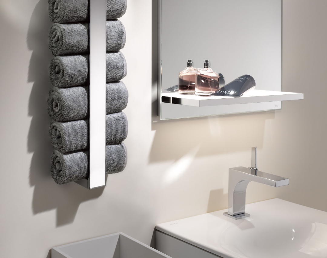 Keuco Edition 400 chrome vertical towel rack with rolled grey towels, featuring a matching basin mixer tap and vanity mirror with shelf.