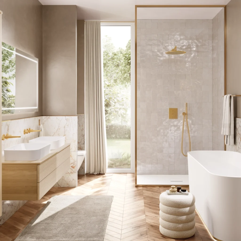 A high-end Villeroy & Boch bathroom suite showcasing a freestanding bathtub and a walk-in shower with pearlescent tiles and gold hardware. The room features a light wood double vanity with marble accents, herringbone timber flooring, and a large window with soft cream drapes.